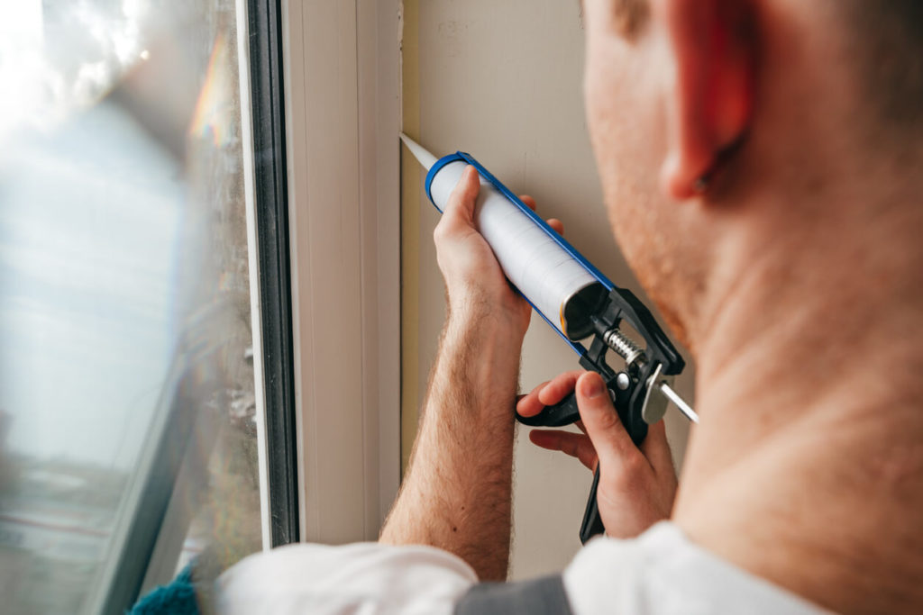 Photo of contractor holding a caulking gun, sealing a window