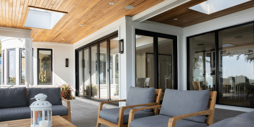 Outdoors on the patio looking back at the black framed windows and sliding doors on the house. 