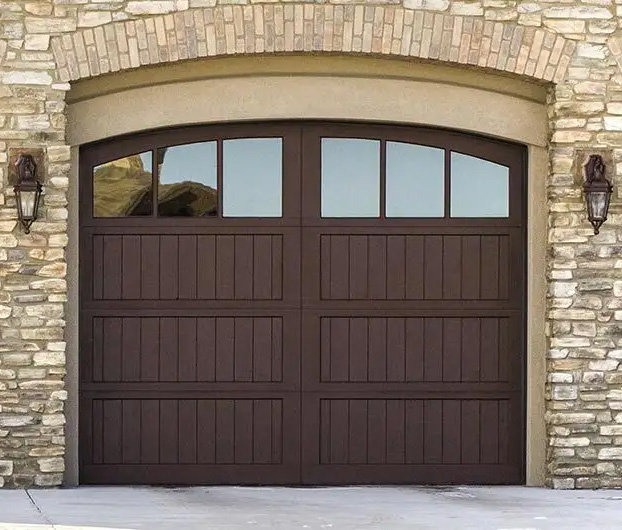 Wood panel garage doors. Three doors in a dark wood finish with a curved window across the top, and stone pillars between.