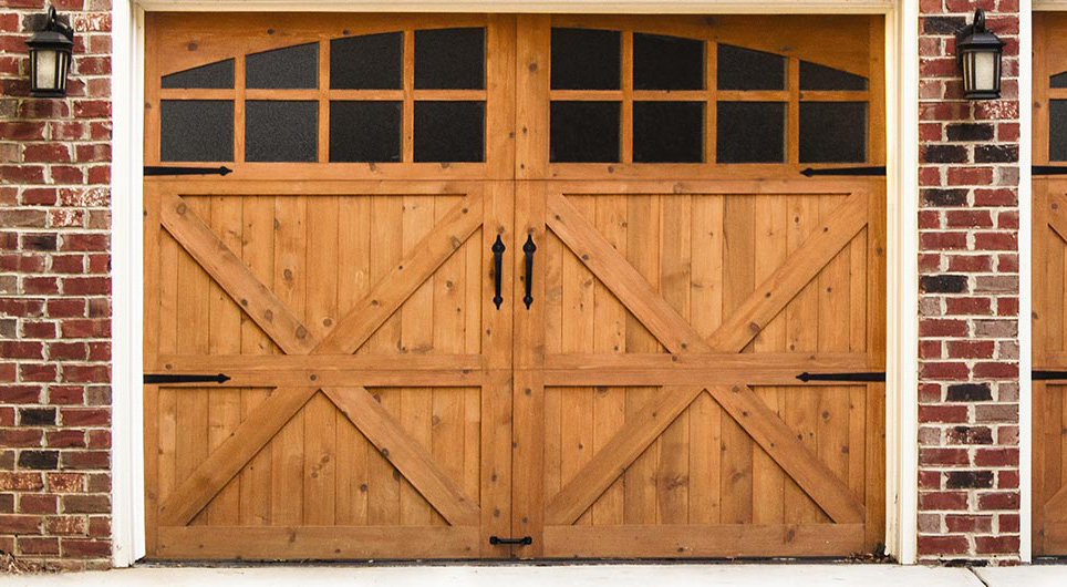 Carriage house style wood garage doors in light wood finish. Double doors with red brick garage.