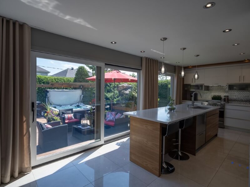 A photo of a lift and slide door in a kitchen, leading out to a deck with a hot tub and patio furniture. 