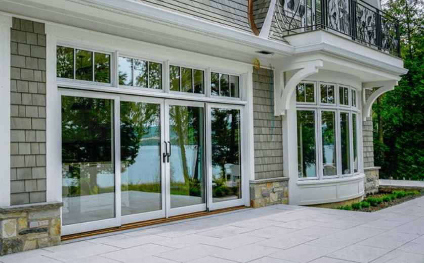 A photo of lift and slide doors with white frames, installed in a house, leading to a stone patio.