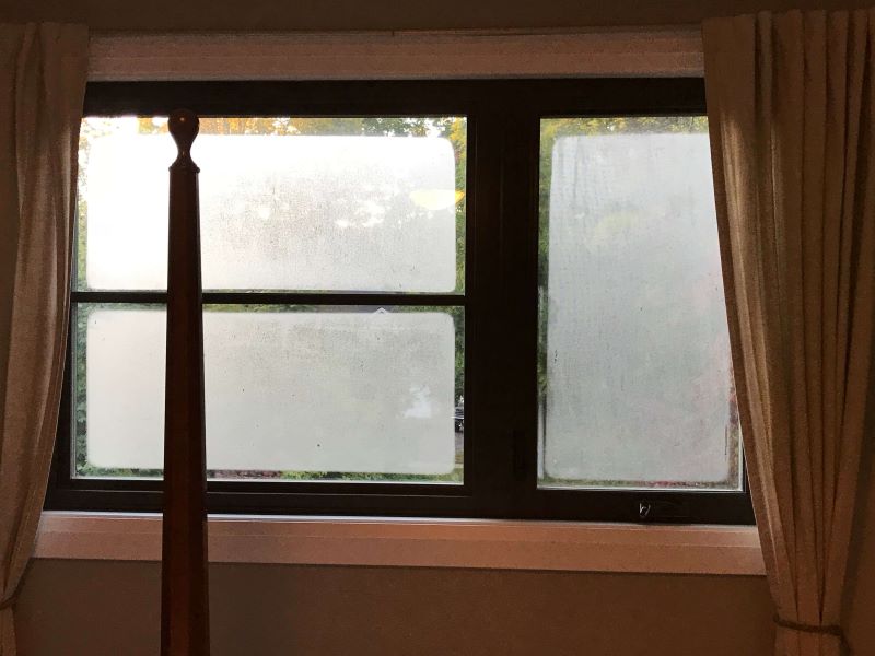 A photo of a window with a black frame, with heavy condensation on the outside of the glass.